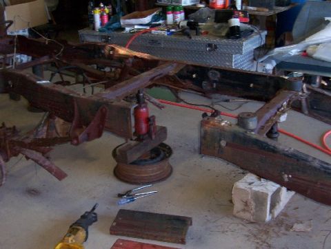 1992 Lincoln Custom - A heavily rusted vehicle frame is disassembled on a workshop floor, surrounded by tools and equipment.