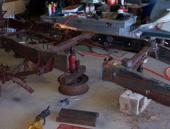 Rusty vehicle frame on concrete floor with tools and a jack