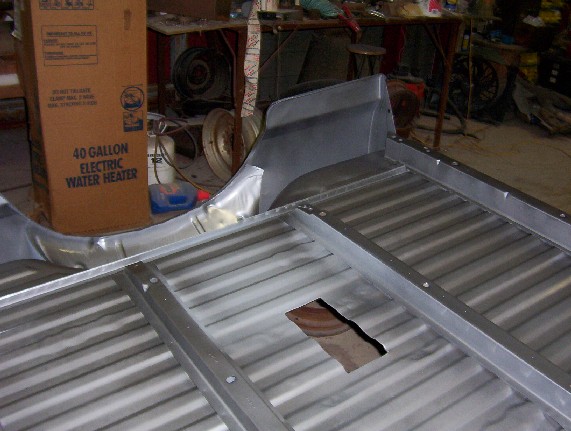Unfinished truck bed with metal floor and sides, showing a large cutout. A box for a 40-gallon electric water heater is visible