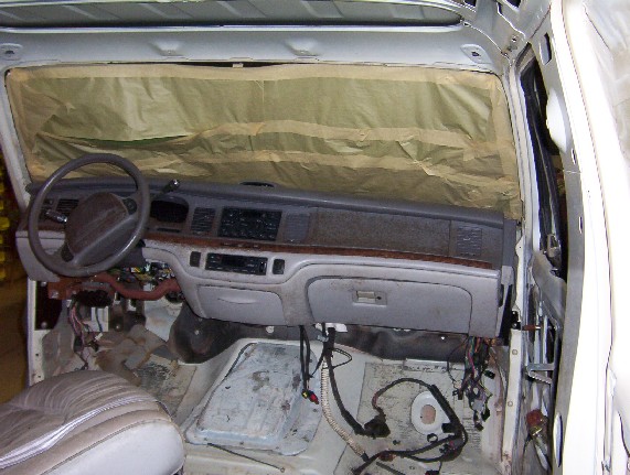 Car interior with dashboard removed, showing exposed wiring and parts. Windshield is covered with paper