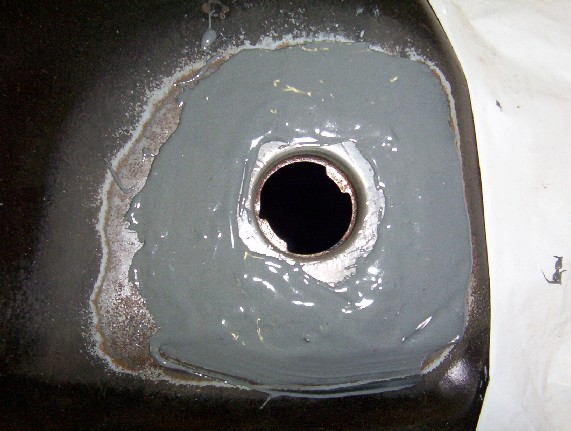 Body panel with cut round hole surrounded by rough gray body filler and bare metal