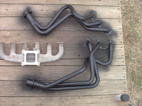 1985 Ford Bronco - Aftermarket Offenhauser intake manifold and exhaust headers laid out on a wooden surface.