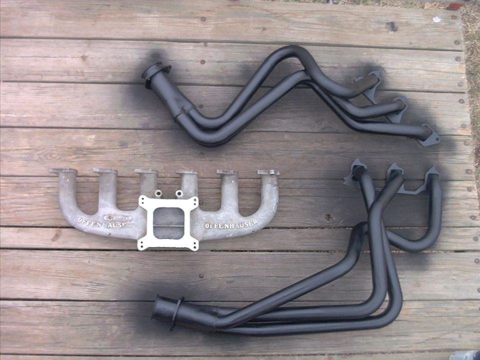 two exhaust manifolds and a set of headers on a wooden surface