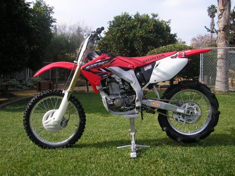 1900 Honda Big Red - A red Honda CRF dirt bike is displayed on a stand outdoors on a sunny day.