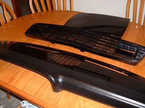 1978 Ford Mustang II - Two black plastic automotive parts, likely a grille and trim, are displayed on a wooden table.