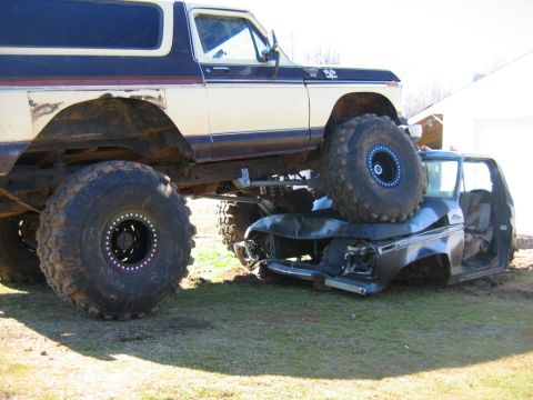 1992 Ford Mustang - A lifted Ford Bronco sits atop a severely damaged pickup truck, demonstrating significant off-road modification.