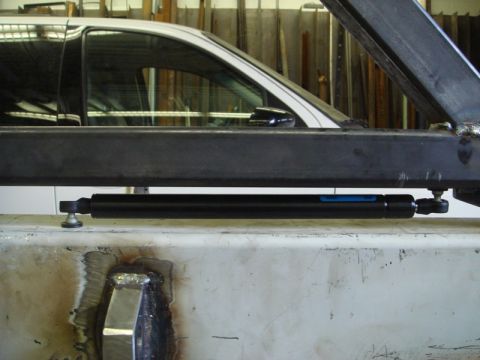 1996 Ford Bronco - Close-up of a gas strut, with a vehicle's side profile visible behind it.