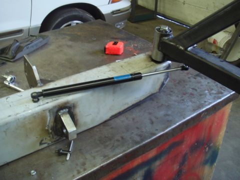 1996 Ford Bronco - A gas strut is mounted to a metal beam on a workbench, with tools and a tape measure visible.