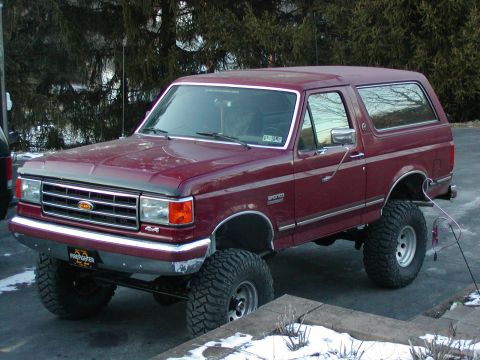 1991 Ford Bronco - Maroon 1991 Ford Bronco, lifted with large off-road tires, sits outside in a snowy environment.