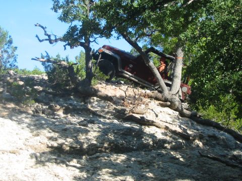 1996 Ford Bronco - A red Jeep Wrangler navigates a challenging off-road trail, with its tires gripping the rocky terrain.