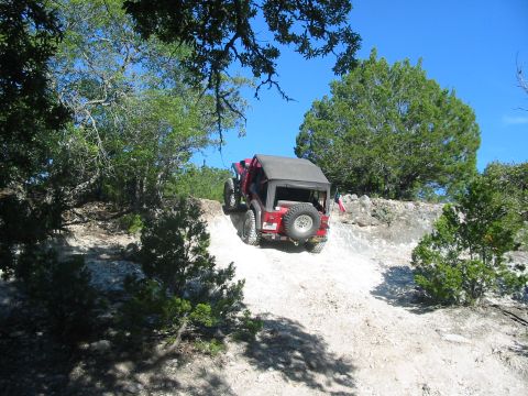 1996 Ford Bronco - A red Jeep Wrangler navigates a steep, sandy incline on a sunny day.