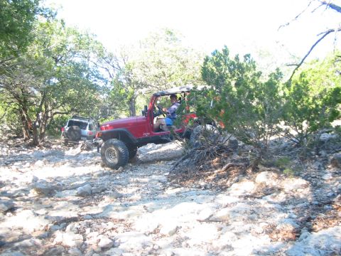 1996 Ford Bronco - Two off-road vehicles navigate a challenging rocky path through a wooded area.