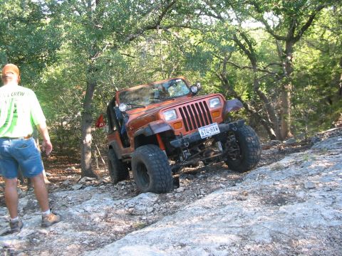 1996 Ford Bronco - An orange Jeep Wrangler navigates a rocky trail, demonstrating its off-road capabilities.