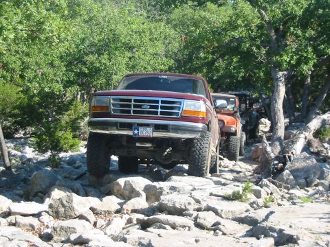 1996 Ford Bronco - Red 1995 Ford F-150 navigates a rocky trail, with an orange Jeep following behind.