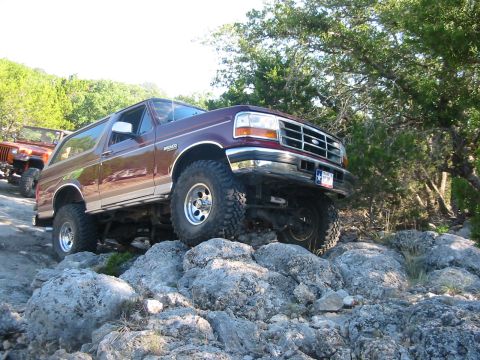 1996 Ford Bronco - A maroon Ford Bronco navigates a rocky trail, with another off-road vehicle visible behind it.