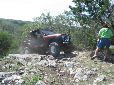1996 Ford Bronco - A red Jeep CJ-7 navigates a challenging rocky terrain with a person in a green shirt watching.