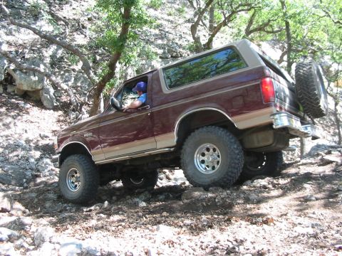 1996 Ford Bronco - This 1996 Ford Bronco is navigating a challenging off-road path through a wooded, rocky area.