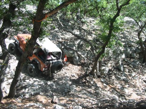 1996 Ford Bronco - An off-road vehicle navigates a steep, rocky incline surrounded by trees and foliage.