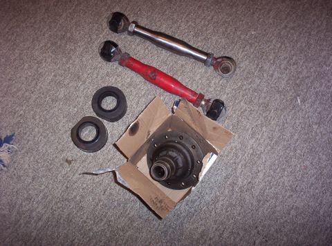 1987 Jeep Cherokee - Automotive suspension parts including a differential, control arms, and bushings are laid out on a carpeted surface.