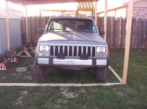 1987 Jeep Cherokee - The front of a Jeep Cherokee is visible, parked in a grassy area with a wooden fence in the background.