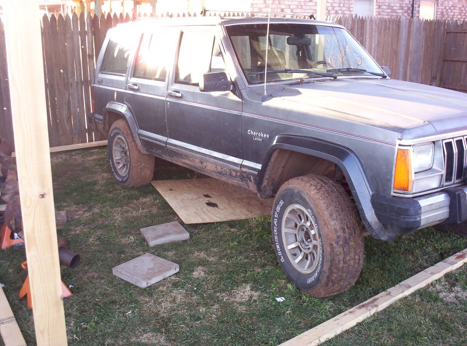 Dark gray Jeep Cherokee with "Cherokee" and "Limited" badges, parked on grass with wooden planks