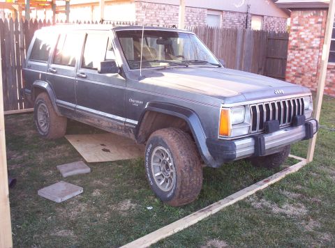 1987 Jeep Cherokee - This 1987 Jeep Cherokee is shown in a three-quarter front view, its dark gray exterior partially obscured by a wooden frame.