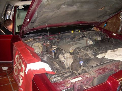 1989 Lincoln Town Car - Mechanic works on the engine of a 1989 Lincoln Town Car, hood fully open.