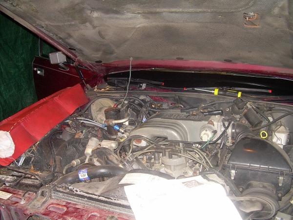 engine bay of a maroon car, hood open, showing engine components and wiring