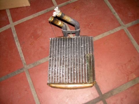 1989 Lincoln Town Car - A used heater core sits on a tiled surface, showing signs of wear and damage to its tubes.