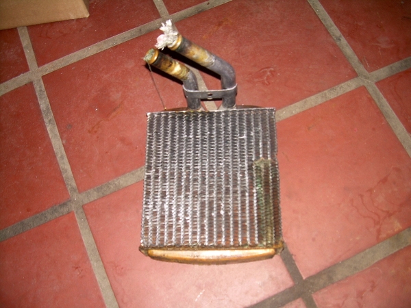 Heater core with two bent metal tubes, one with frayed rope. The fins are dirty and corroded