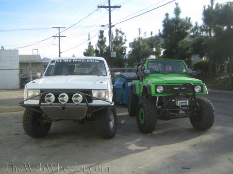1990 Ford Bronco - white lifted pickup with light bar sits beside a bright green lifted Suzuki off-roader on a paved lot.