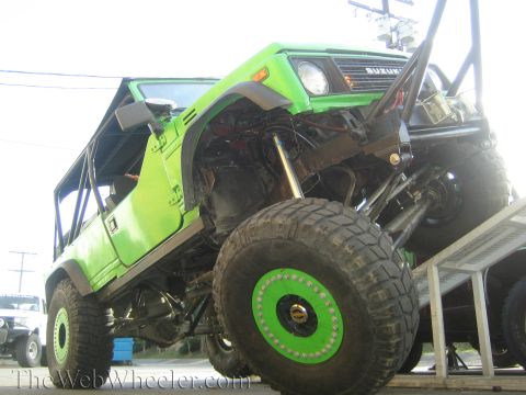 1990 Ford Bronco - Low-angle front view of a green lifted Suzuki off-roader with its raised front end exposing the suspension and axle.
