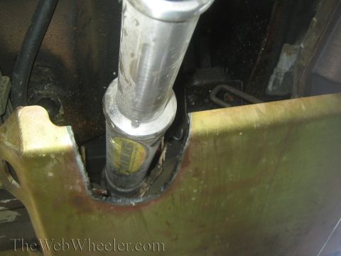 1990 Ford Bronco - Close-up of a polished aluminum shaft passing through a yellow-painted steel bracket beneath a vehicle.