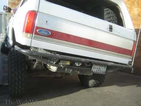 1990 Ford Bronco - Close-up of the rear tailgate of a white lifted Ford Bronco showing the Ford emblem, red stripe, and California license plate.