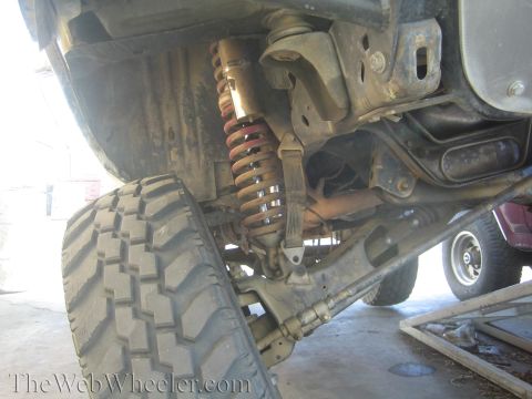 1990 Ford Bronco - Detailed undercarriage view showing a red-coiled coil-over shock, control arm, axle, and driveshaft on a lifted vehicle.