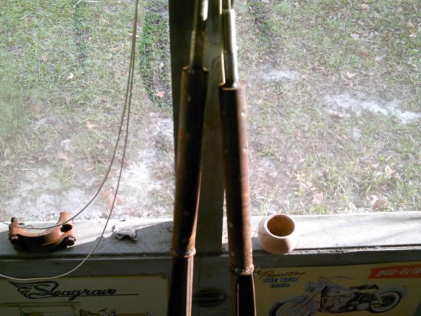 Two rusty metal rods hang in front of a window showing grass and a sign with a motorcycle