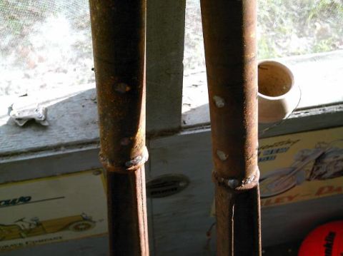 1986 Ford Bronco - Close-up view of two rusty metal pipes, likely parts, indoors.