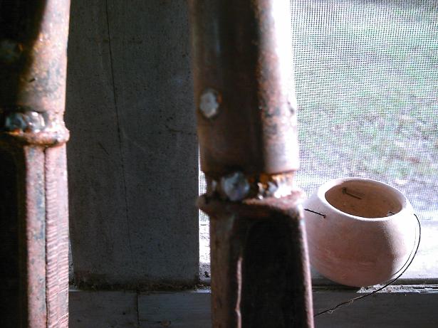 Close-up of two rusted metal posts with visible welds, next to a small terracotta pot on a windowsill