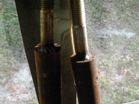 1986 Ford Bronco - Close-up view of two metal rods, possibly part of a vehicle's suspension system, with visible bolts and threaded ends.