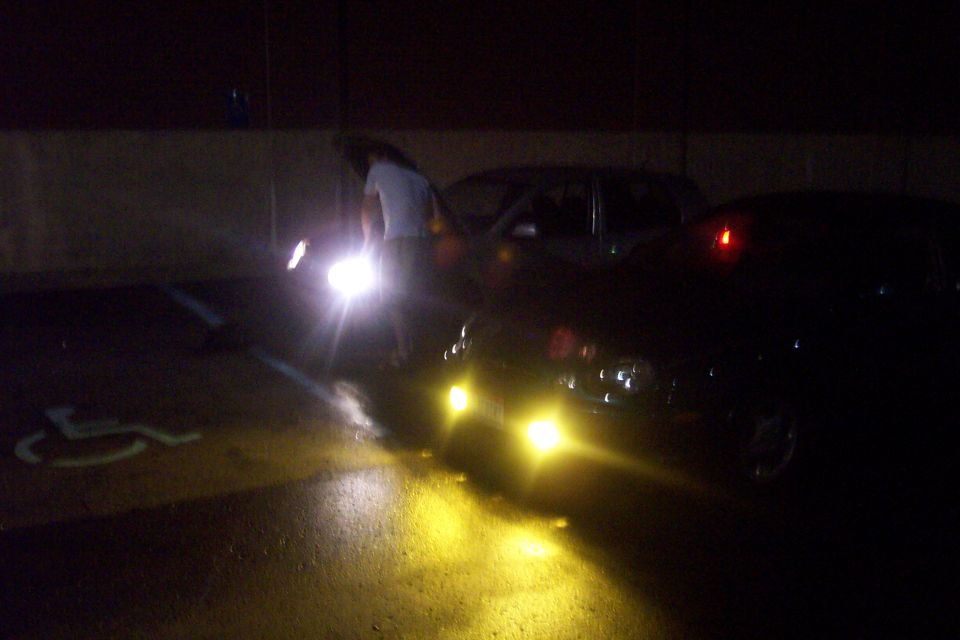 Dark sedan with yellow fog lights parked at night in a lot near a handicap space, person at open door