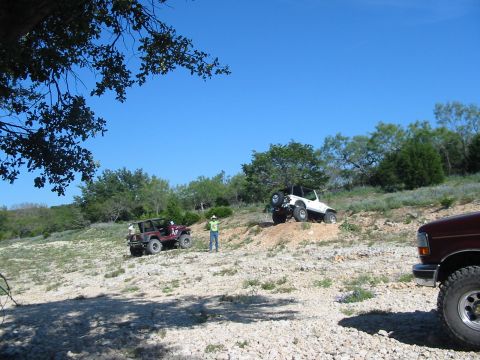 1996 Ford Bronco - Several off-road vehicles navigate a challenging, rocky terrain under a clear blue sky.