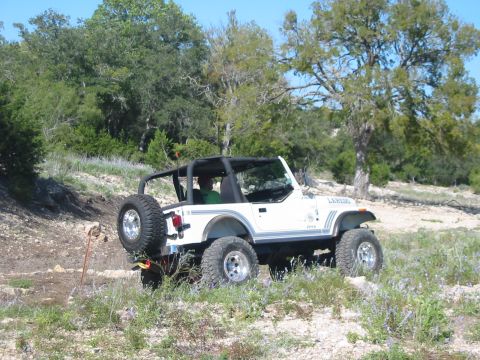 1996 Ford Bronco - A white Jeep Wrangler navigates a , outdoor terrain with sparse vegetation and trees.