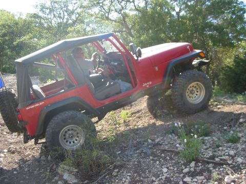 1996 Ford Bronco - A red Jeep Wrangler navigates a rocky trail, demonstrating its off-road capabilities.
