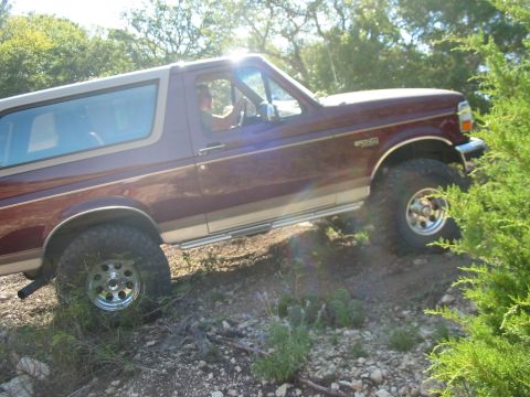 1996 Ford Bronco - 1996 Ford Bronco navigating an off-road trail with a driver visible.
