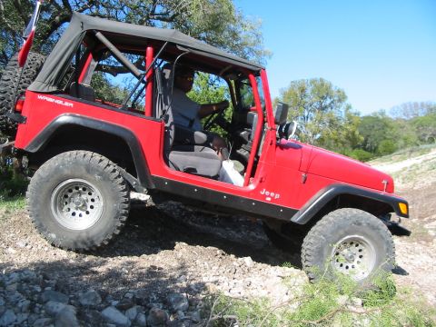 1996 Ford Bronco - A red Jeep Wrangler navigates a rough, rocky terrain under a clear blue sky.