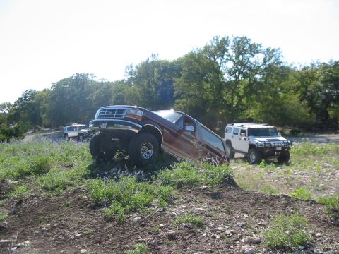 1996 Ford Bronco - A maroon 1996 Ford Bronco navigates an off-road incline, with a white SUV visible in the distance.