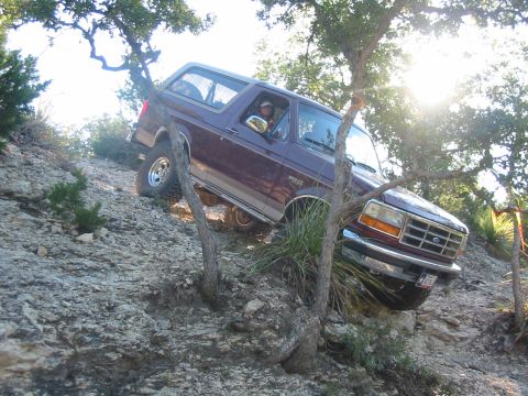 1996 Ford Bronco - This Ford Bronco is navigating a steep, rocky incline surrounded by trees and brush.