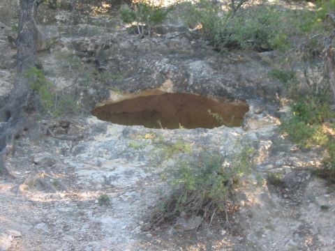 1996 Ford Bronco - A natural cave opening is visible in a rocky hillside, surrounded by dry brush and trees.