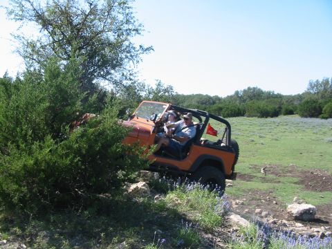 1996 Ford Bronco - Two people are off-roading in an orange Jeep Wrangler on a sunny day.