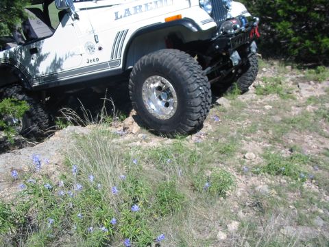 1996 Ford Bronco - White Jeep CJ-7 Laredo with aftermarket wheels and tires navigating rough terrain.